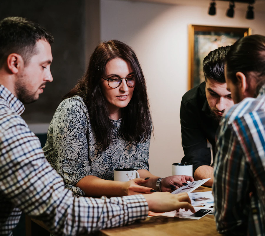 Four colleagues leaning over a table, reading printed pages; one points at a line.